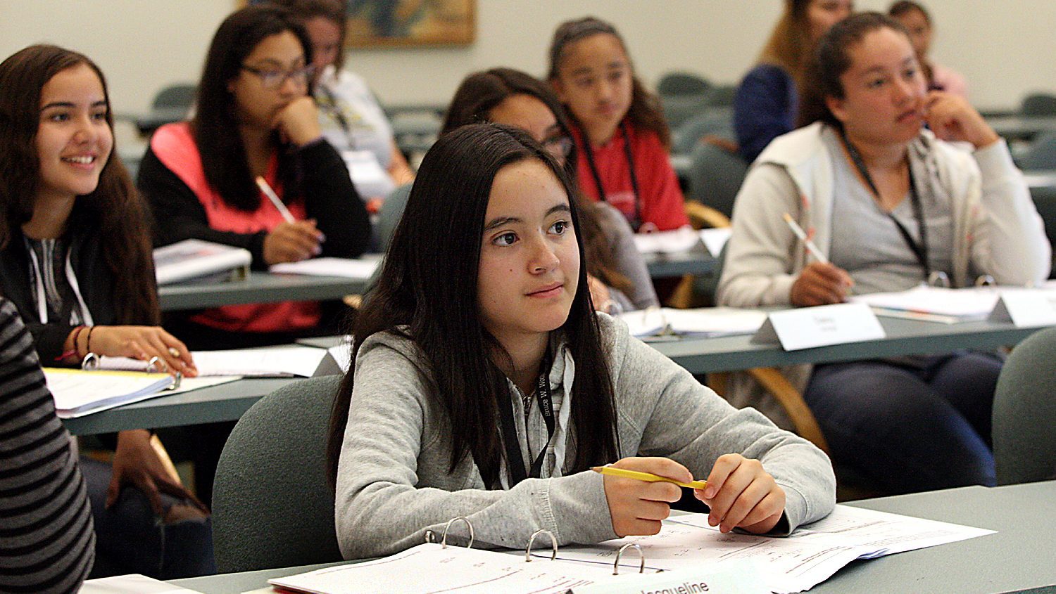 Young girl holding pencil sitting in classroom smiling